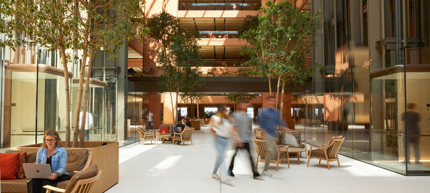 The lower floor of the light-filled Battersea atrium with multiple Apple team members meeting, walking and working in various seating arrangements.