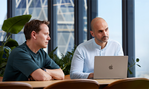 Ahmed, with his MacBook in front of him, sitting at a table with a colleague and looking at someone out of frame.