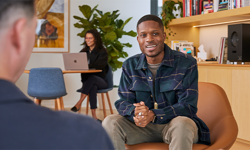 Justin sitting indoors in an office lounge, speaking with an Apple colleague.