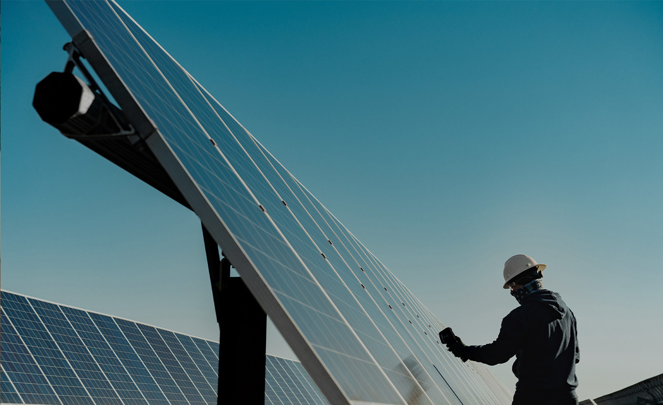 Ein Mann mit Schutzhelm arbeitet im Freien an einem großen Solarpanel. 