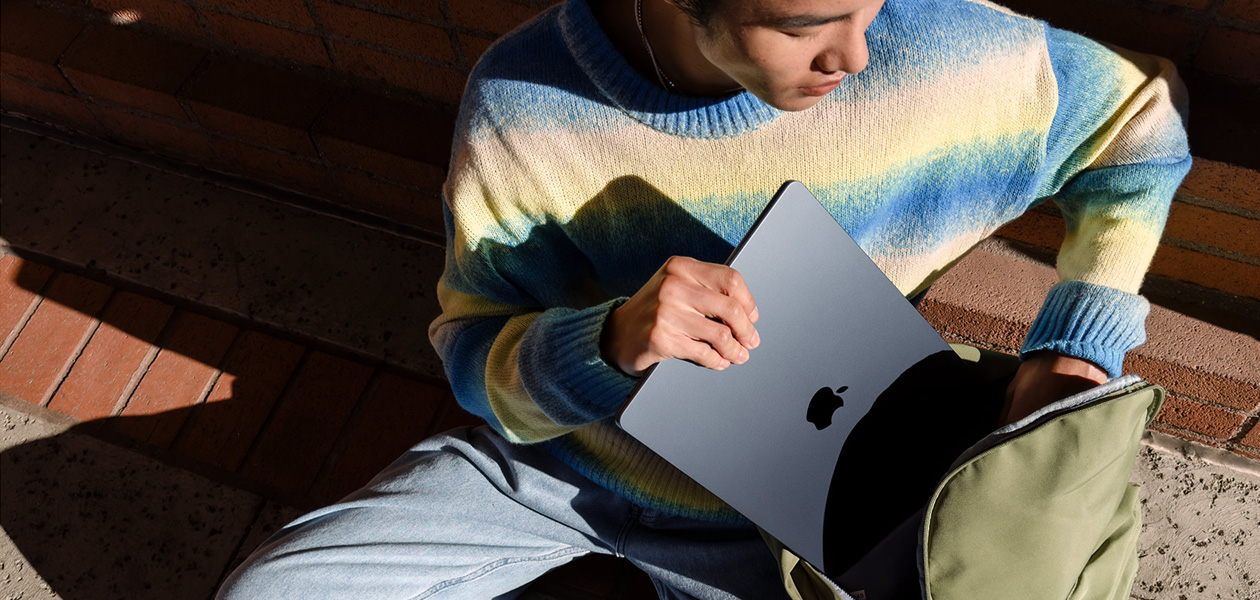 屋外で座っている学生がバックパックからMacBook Airを取り出している。